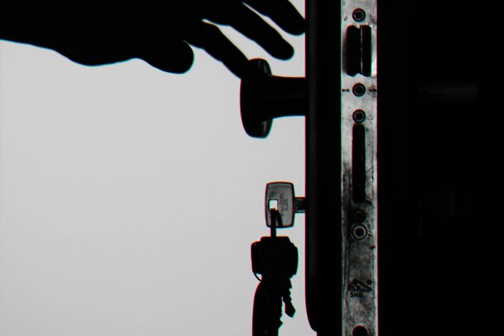 Silhouette of a hand about to open a door with keys in lock, symbolizing security.