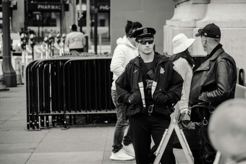 A police officer on patrol in an urban street, engaging in conversation, captured in black and white.